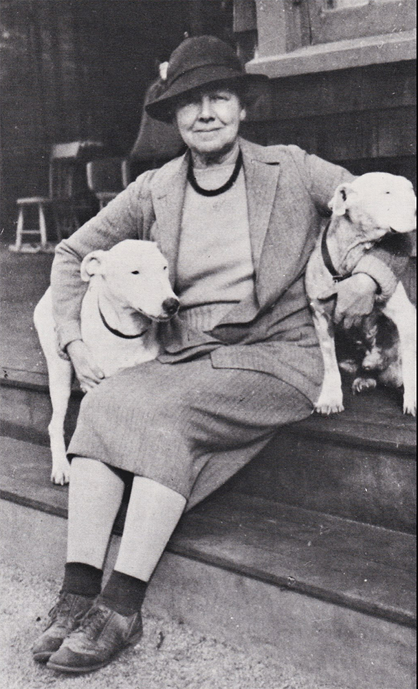 Photograph of Gertrude Fiske seated on porch steps with dogs