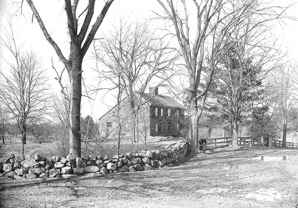 Historic photo of One Chestnut Street showing saltbox house with trees, stone wall, lawn in foreground